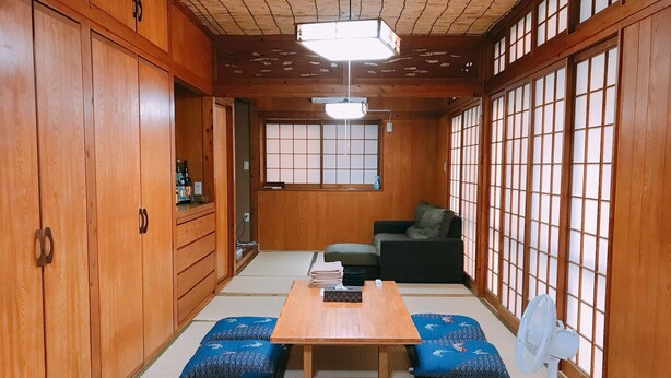 Una habitación japonesa tradicional con suelo de tatami, una mesa baja de madera, un sofá y puertas correderas con un diseño de cuadrícula.