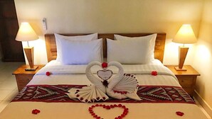 A hotel room with a neatly made bed, two bedside lamps, and a decorative swan made of towels on the bed. - Ayuna Family Ubud (Ubud)