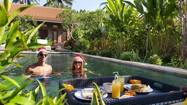 A poolside setting with two people in the water, a dining table with food and drinks, and lush greenery. - Ayuna Family Ubud (Ubud)