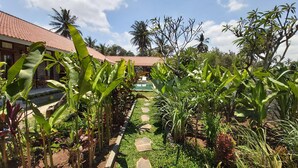 A garden with a pathway leading to a building with a red roof. - Ayuna Family Ubud (Ubud)