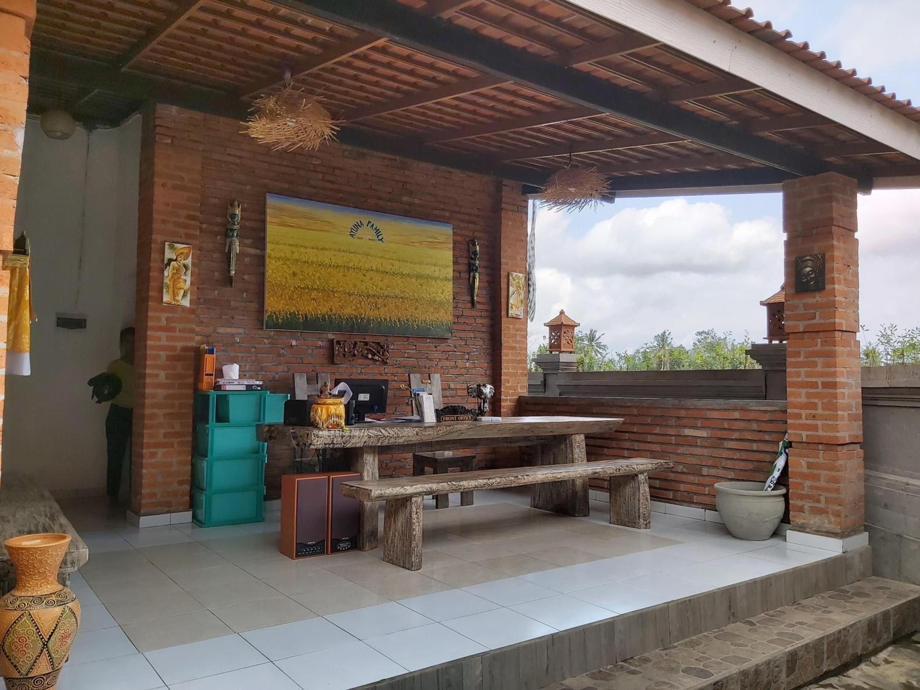 Une terrasse extérieure avec une table et un banc en bois, un mur en briques et un grand tableau représentant un champ.