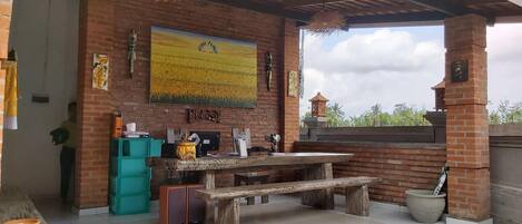 Une terrasse extérieure avec une table et un banc en bois, un mur en briques et un grand tableau représentant un champ.
