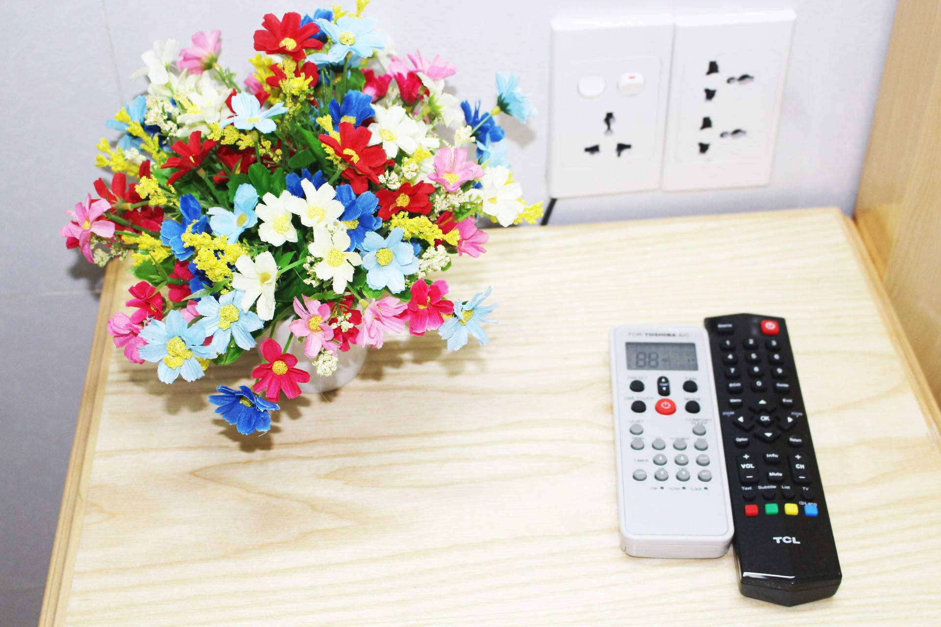 A wooden table with a vase of colorful flowers and two remote controls.