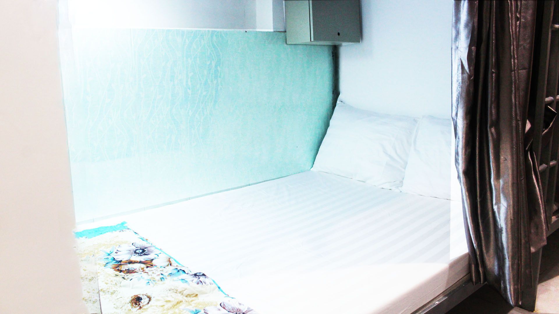A single bed with a white mattress and pillows, a light blue headboard, and a small bedside table with a lamp.