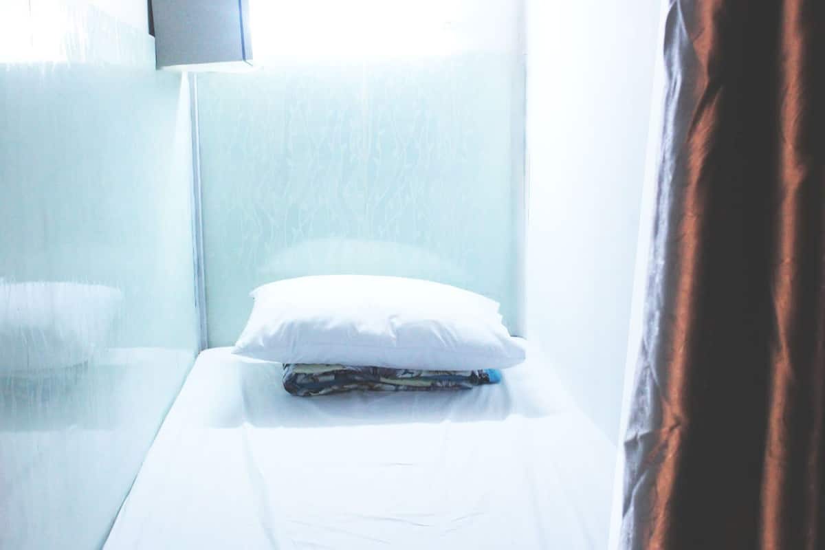 A small, single-bed room with a white bedspread, a white pillow, and a folded blanket.