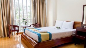 A hotel room with a wooden bed, a wooden nightstand, a chair, a small table with a vase of flowers, and a large window with curtains. - Saigon City Center - Hostel (Ho Chi Minh City)