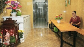A reception area with a marble floor, a wooden reception desk, a green basket, and a statue with flowers. - Saigon City Center - Hostel (Ho Chi Minh City)