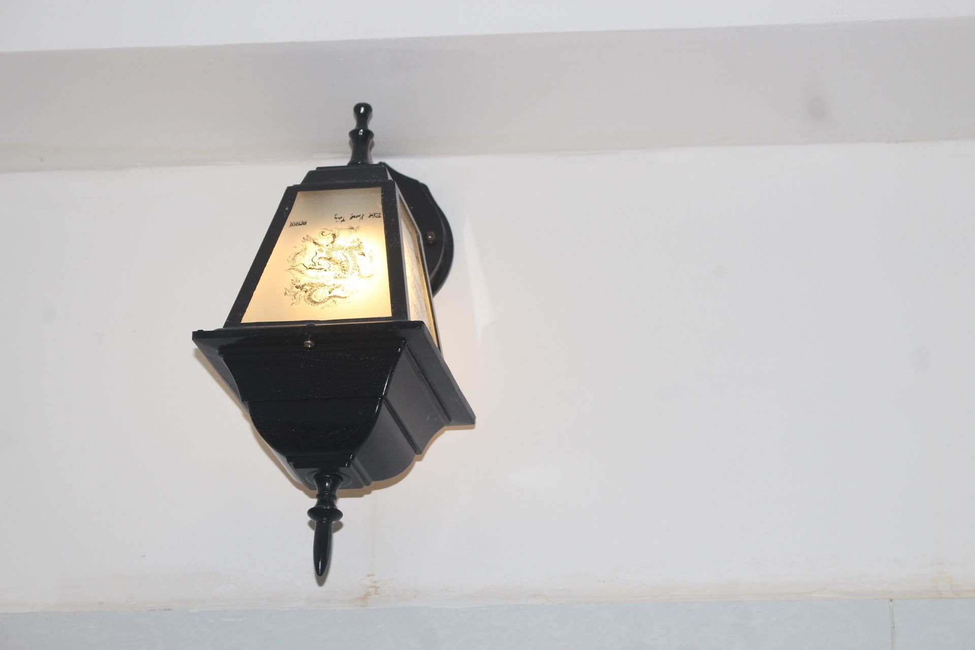 Une lanterne noire, fixée au mur, ornée d’un motif décoratif sur sa façade.