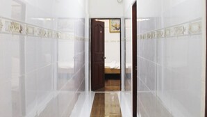 A hallway with white tiled walls and a wooden floor, leading to a bedroom with a bed and a painting on the wall. - Saigon City Center - Hostel (Ho Chi Minh City)