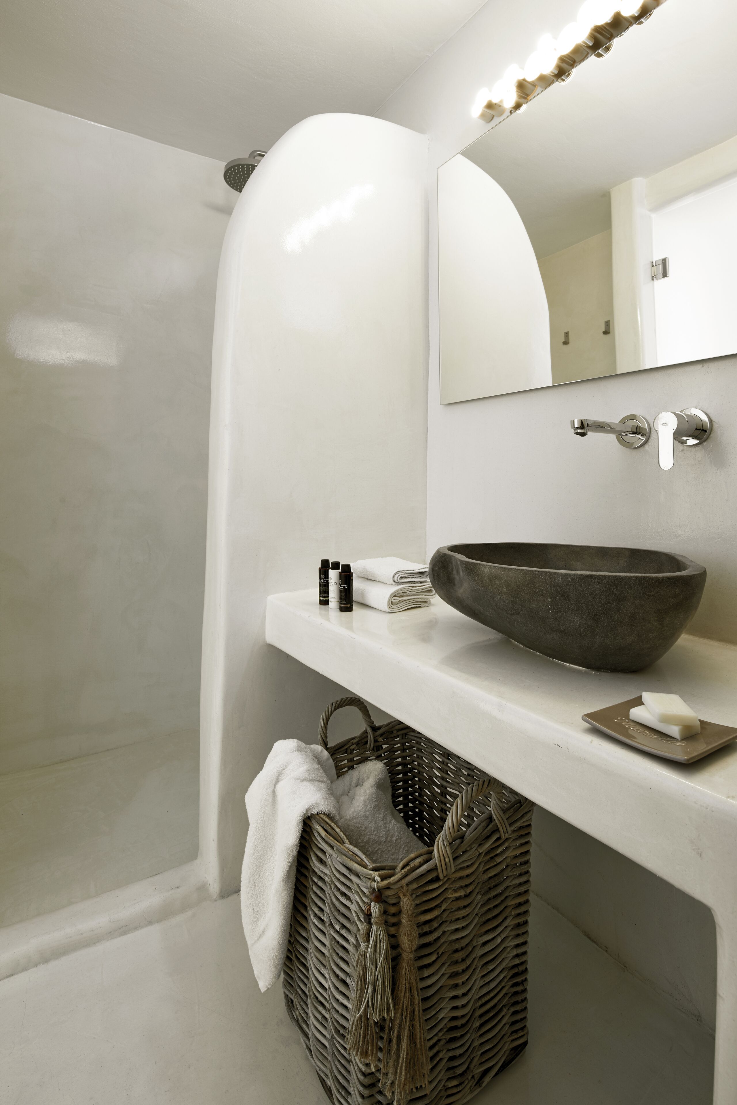 Une salle de bain avec un meuble-lavabo blanc, un grand miroir, un lavabo sur colonne et un panier en osier.