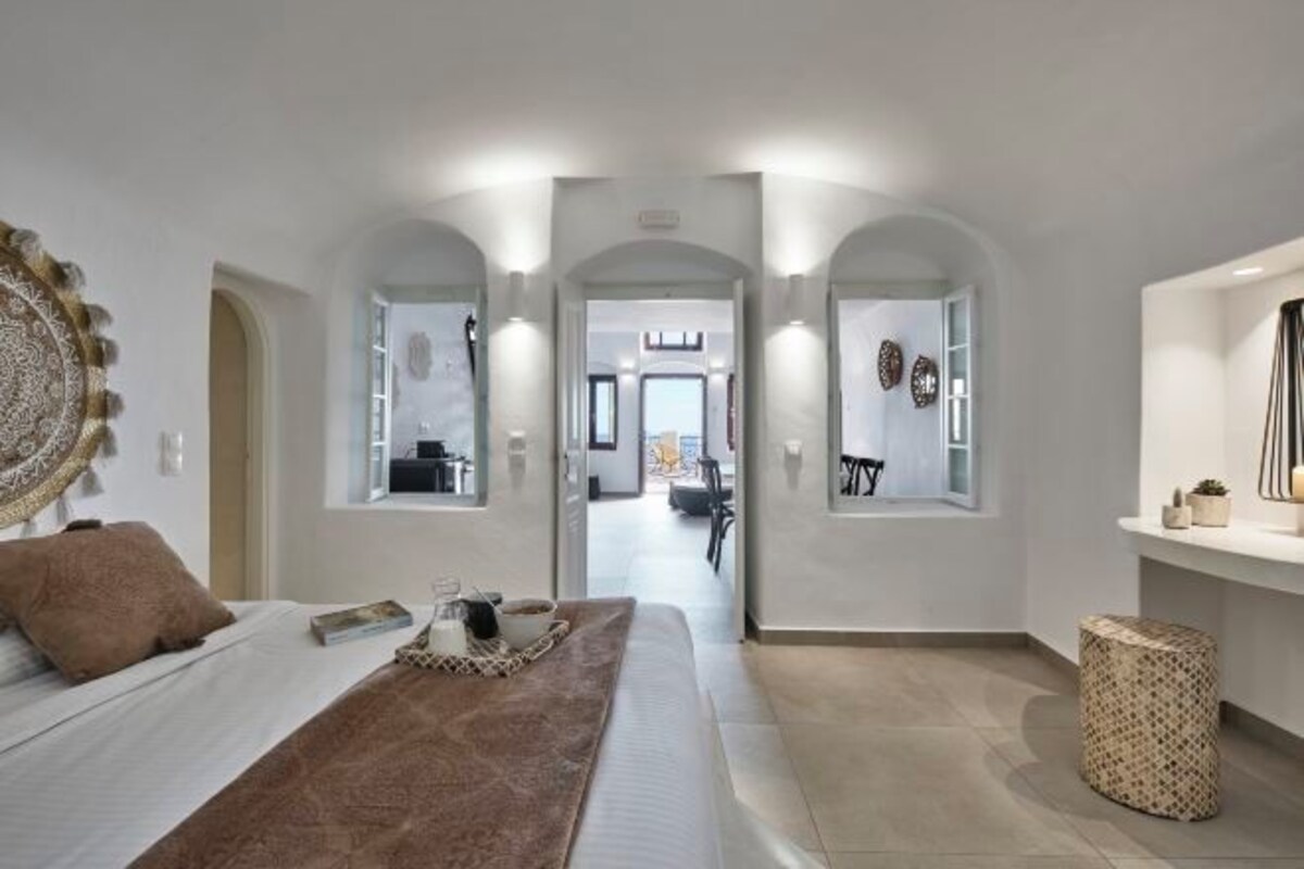 Una moderna camera d'albergo con un letto, un tavolino, uno specchio decorativo e vista sulla stanza adiacente.