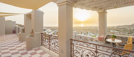 A terrace with a checkered floor, a pergola, and a view of the sunset over a cityscape.