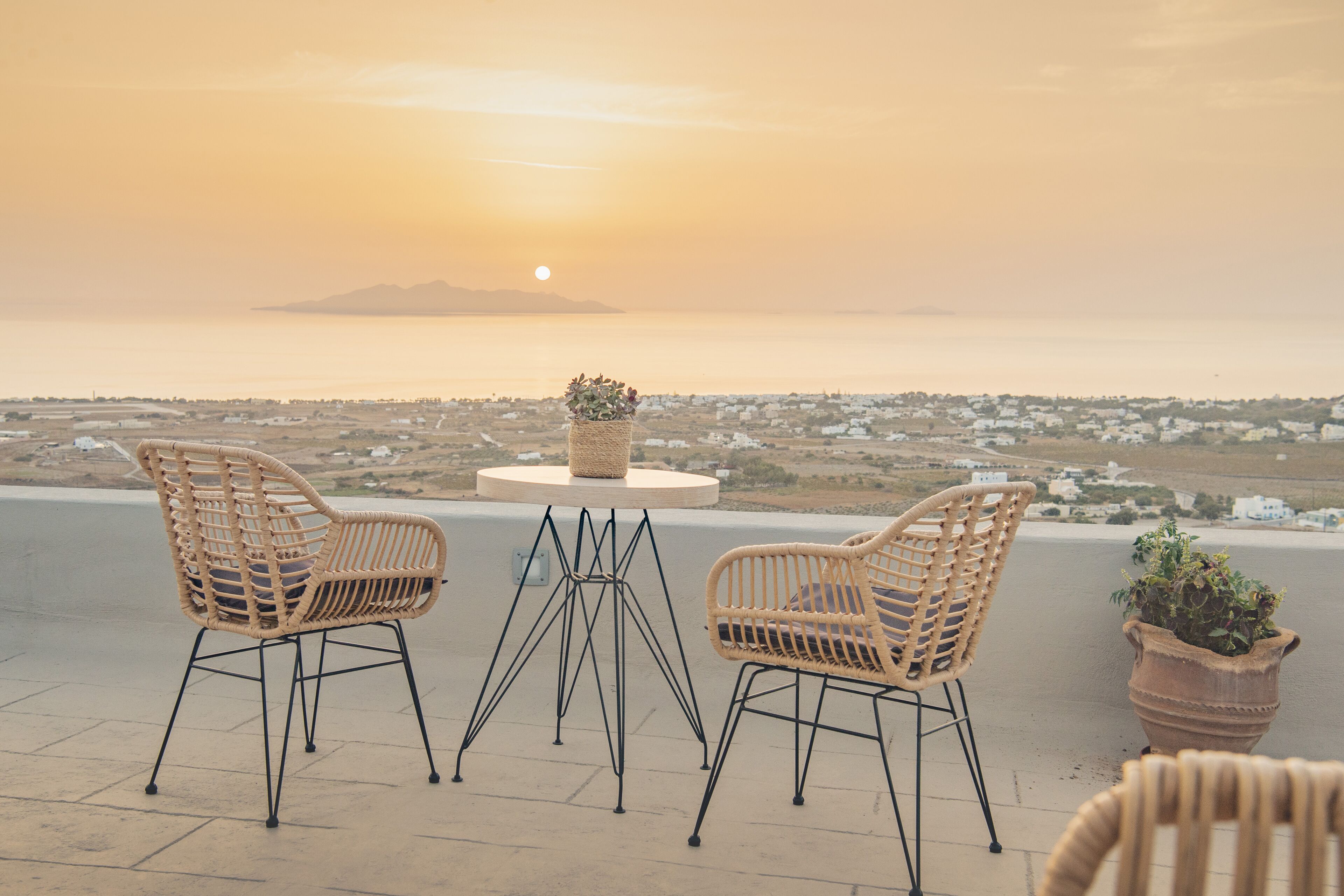 Eine Terrasse mit Korbstühlen und einem Tisch, mit Blick auf eine Küstenstadt und das Meer.