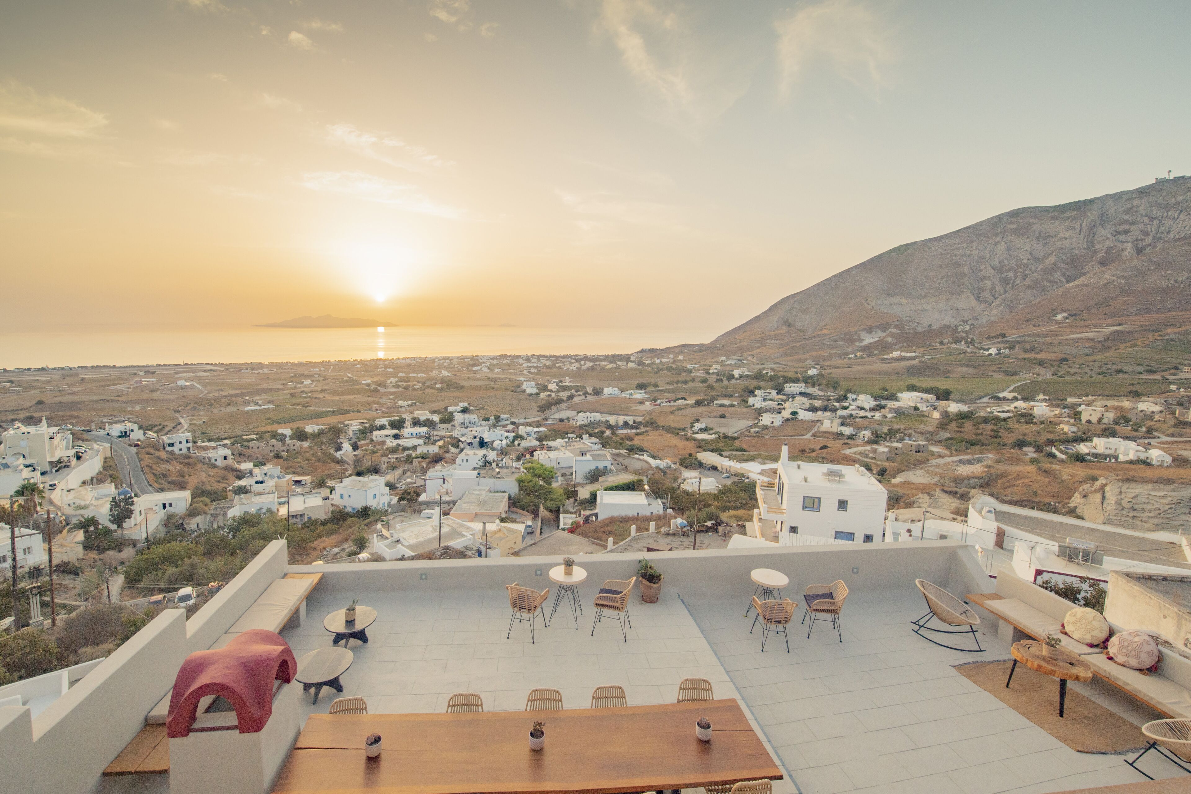 Une terrasse sur le toit, avec des sièges en plein air, offrant une vue sur une ville côtière au coucher du soleil.