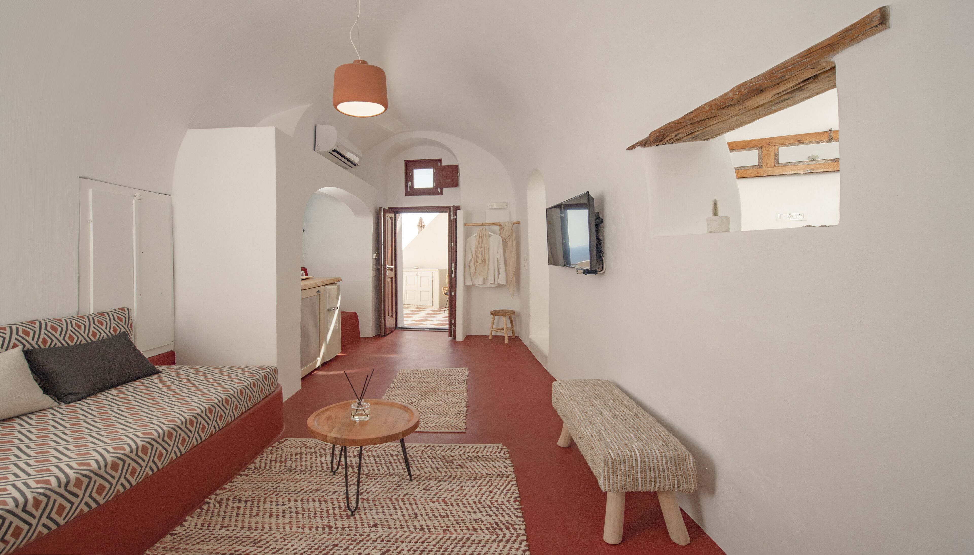 A narrow hallway with a sofa, a bench, a small table, and a TV mounted on the wall.