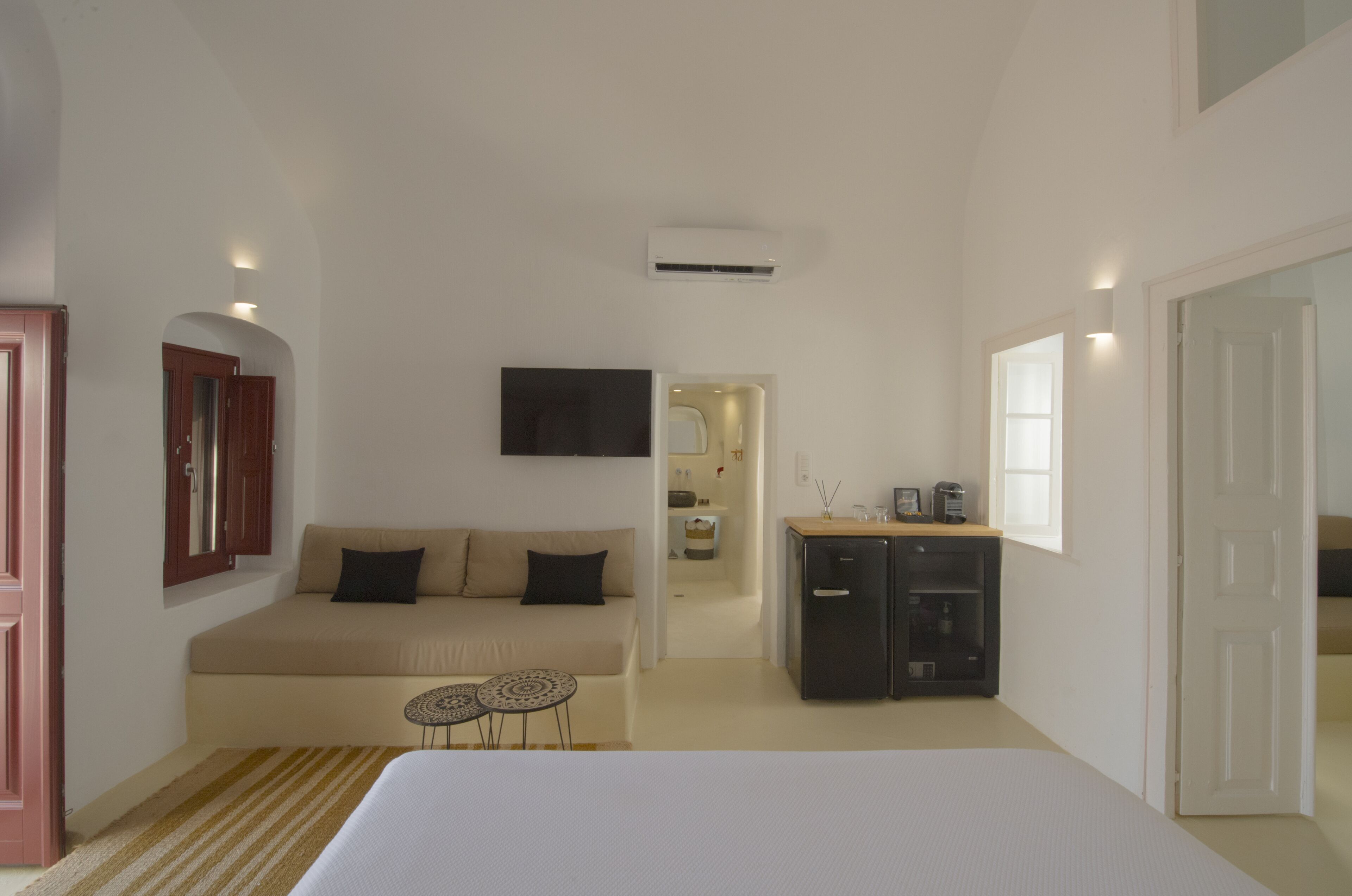 A bedroom with a bed, a sofa, a small table, a TV, and a kitchenette area.