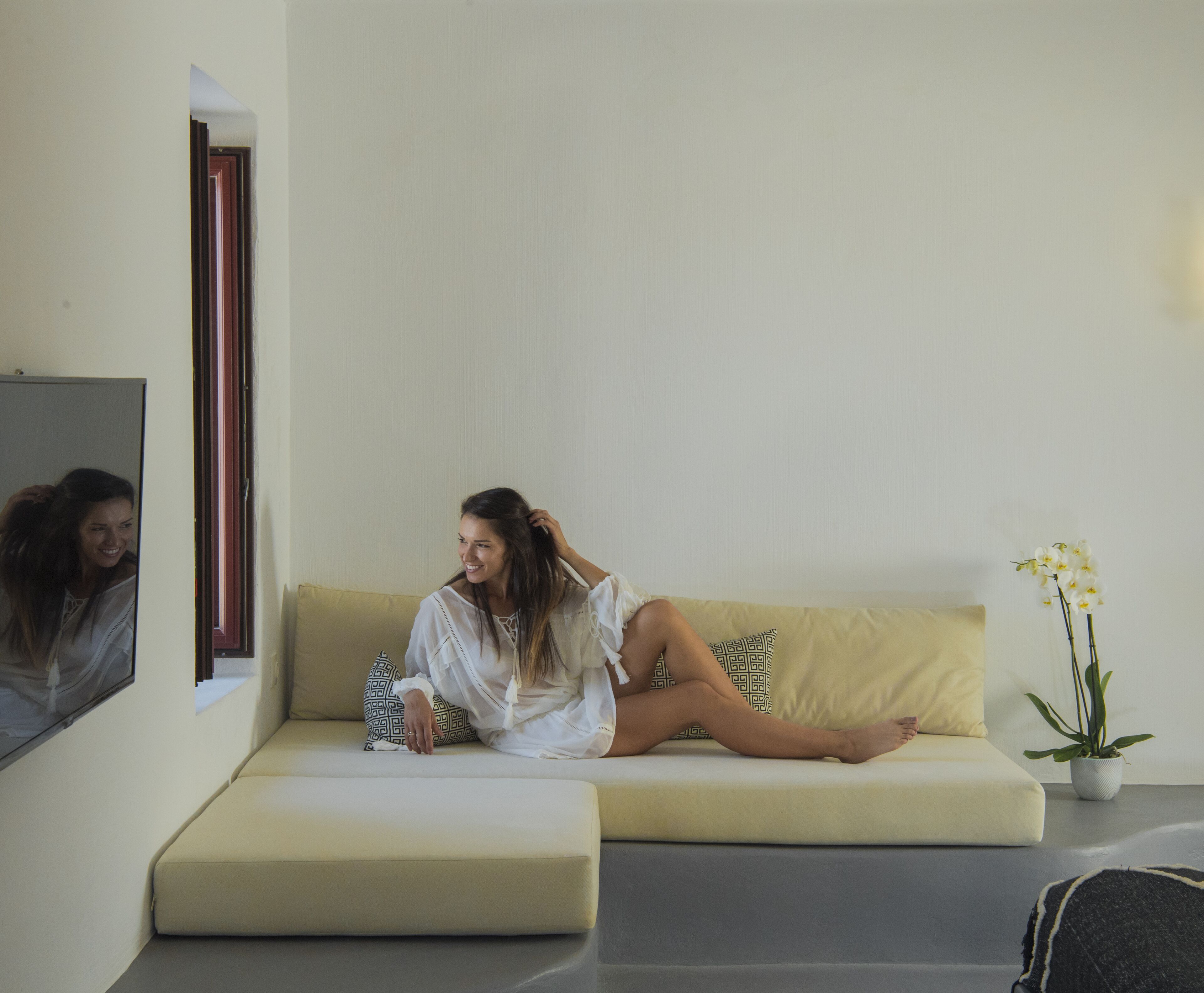 A woman sitting on a sofa in a room with a mirror, a potted plant, and a small table.