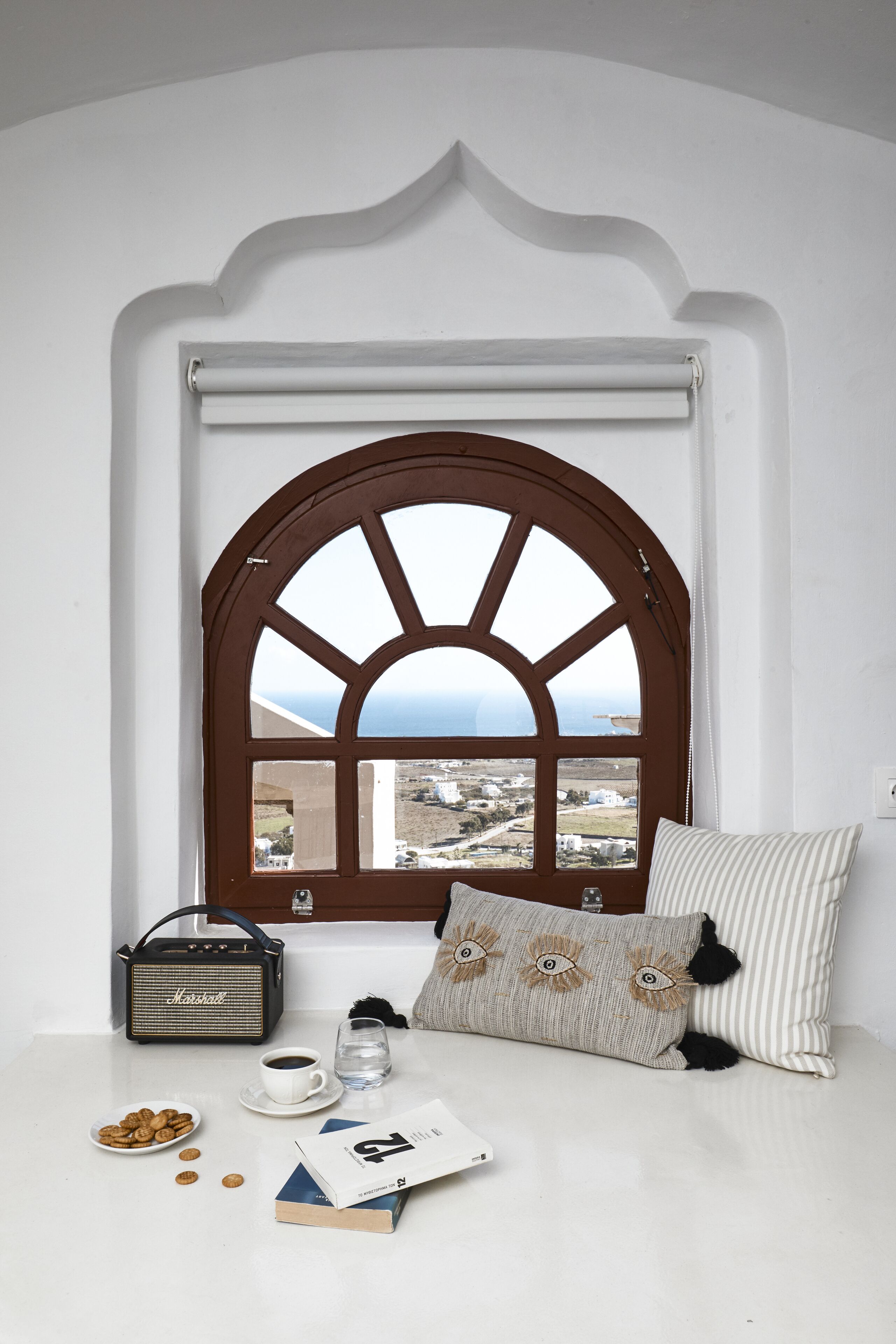 A cozy room with a large arched window, a small table with a radio, a cup of coffee, a plate of cookies, and a book.