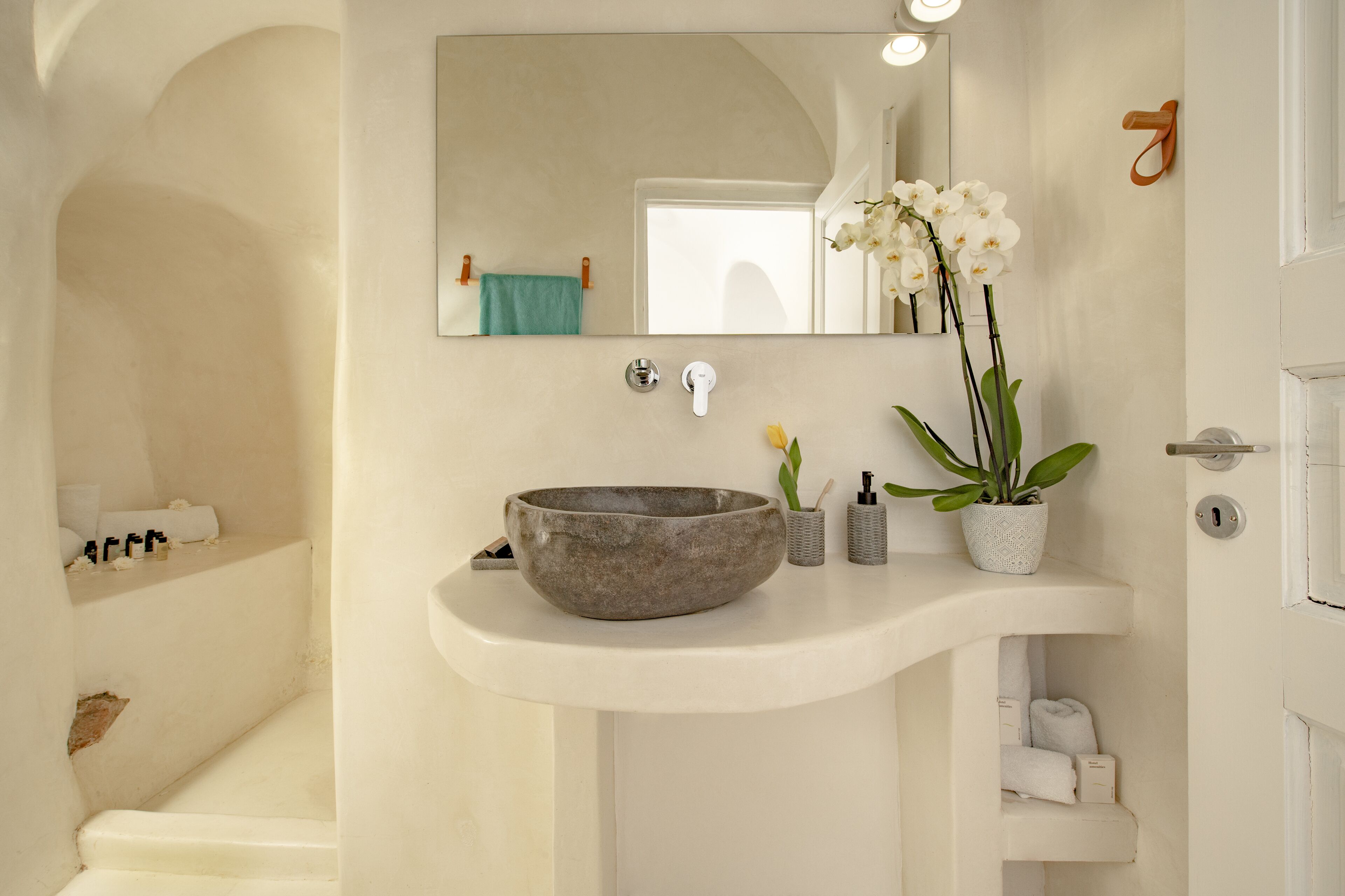 A bathroom with a large mirror, a stone basin, a potted orchid, and a towel rack.