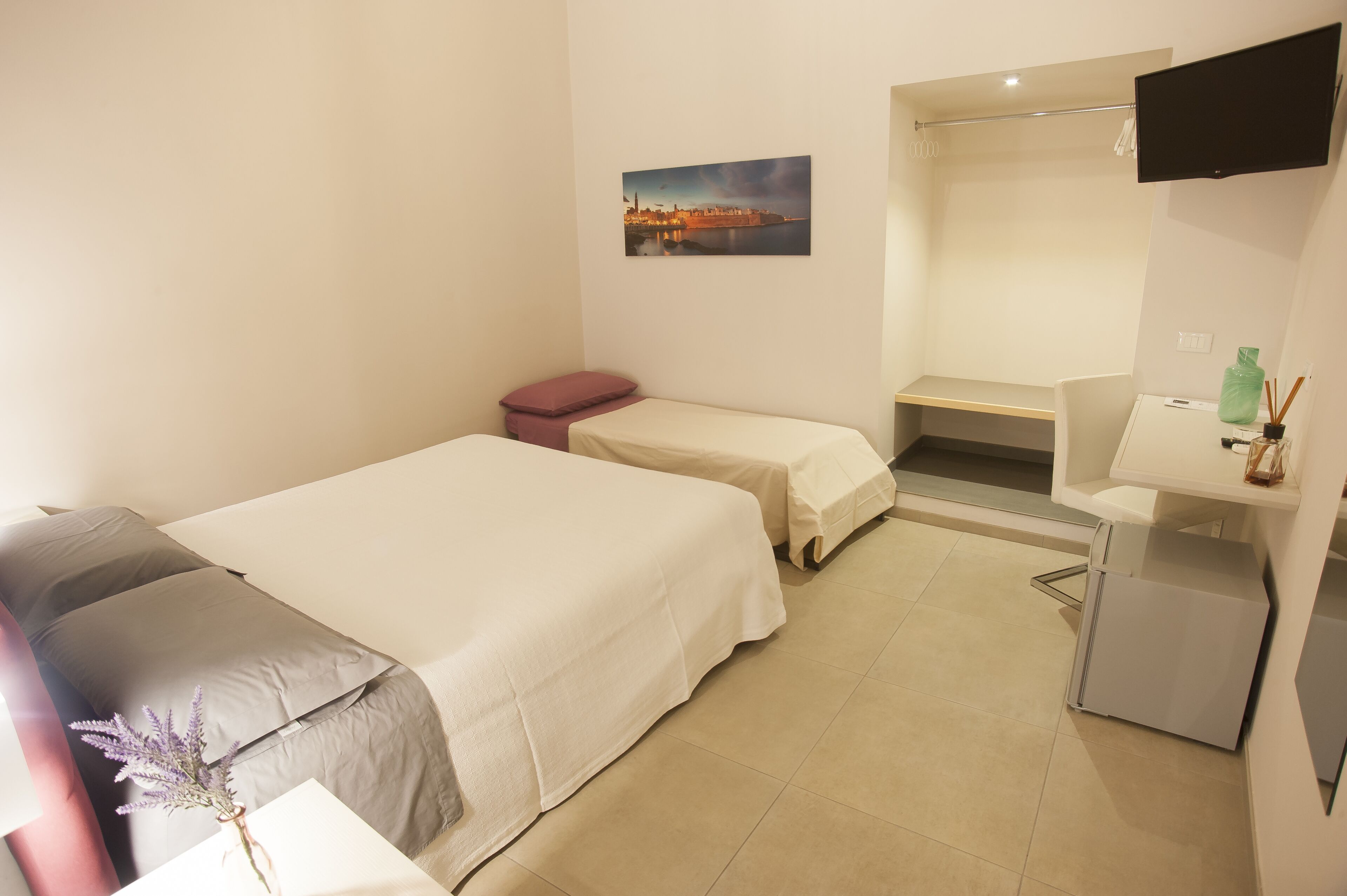 A hotel room with two beds, a small desk, a mirror, and a TV.