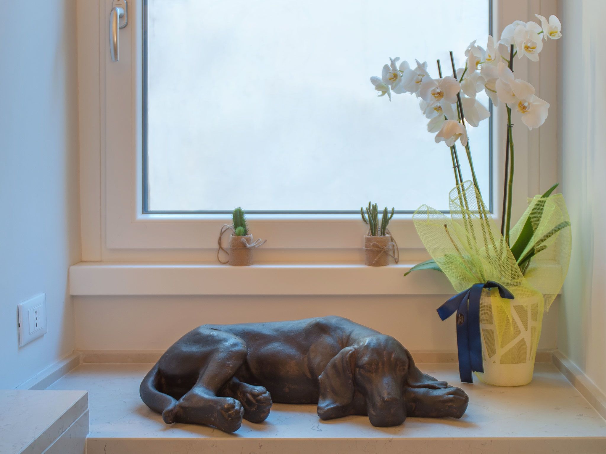 A window sill with a dog sculpture, a cactus, and orchids.