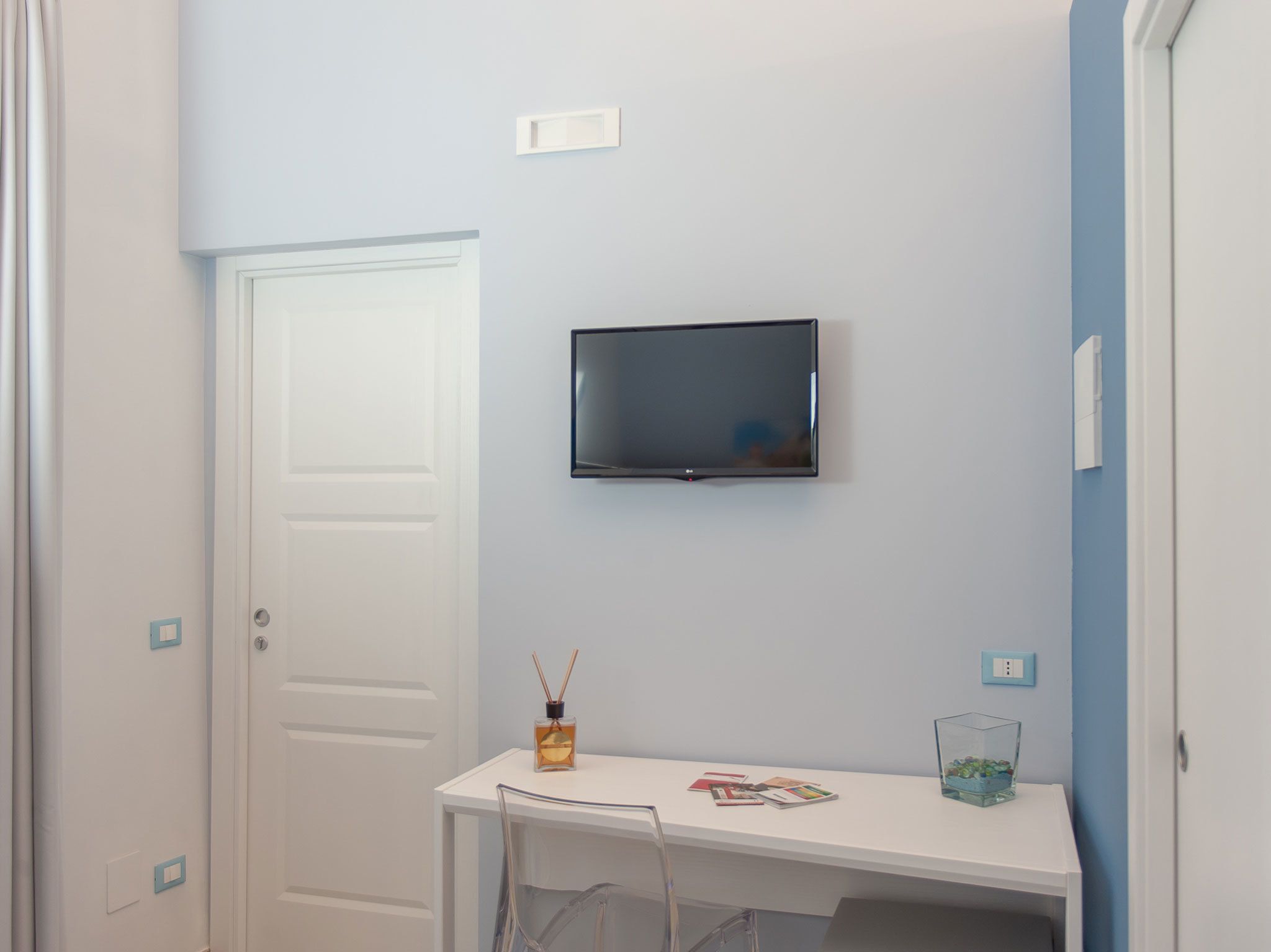 A small room with a white desk, a mounted TV, and a door.