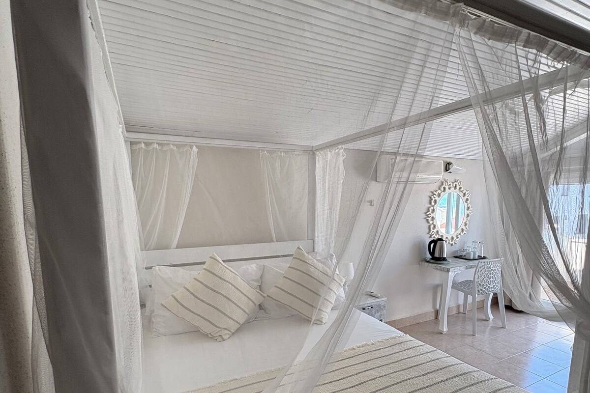 Un lit à baldaquin, une petite table avec une chaise et un miroir au mur.