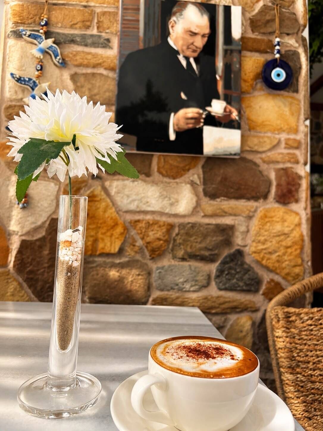 Een tafel met een witte bloevas, een kop koffie en een achtergrond van een stenen muur.