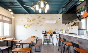 A dining area with wooden tables and benches, a bar counter with stools, and a ceiling fan. - Liuqiu Backpackers Hostel (Liuqiu)