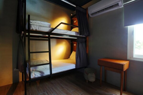 Une chambre avec un lit superposé, un plancher en bois, une petite table et un appareil de climatisation.