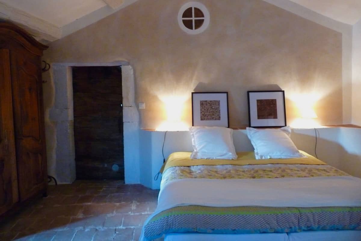 Een slaapkamer met een bed, twee wandlampen, een houten garderobe en een stenen vloer.
