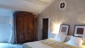 A bedroom with a large wooden wardrobe, a bed with white bedding, and two framed pictures on the wall.