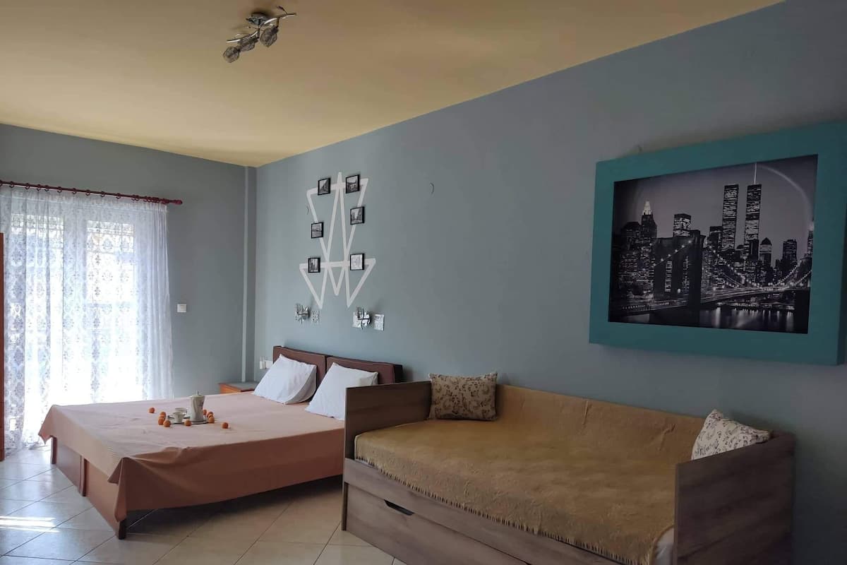 Quarto com cama, sofá, pintura de paisagem urbana e uma instalação de arte na parede.