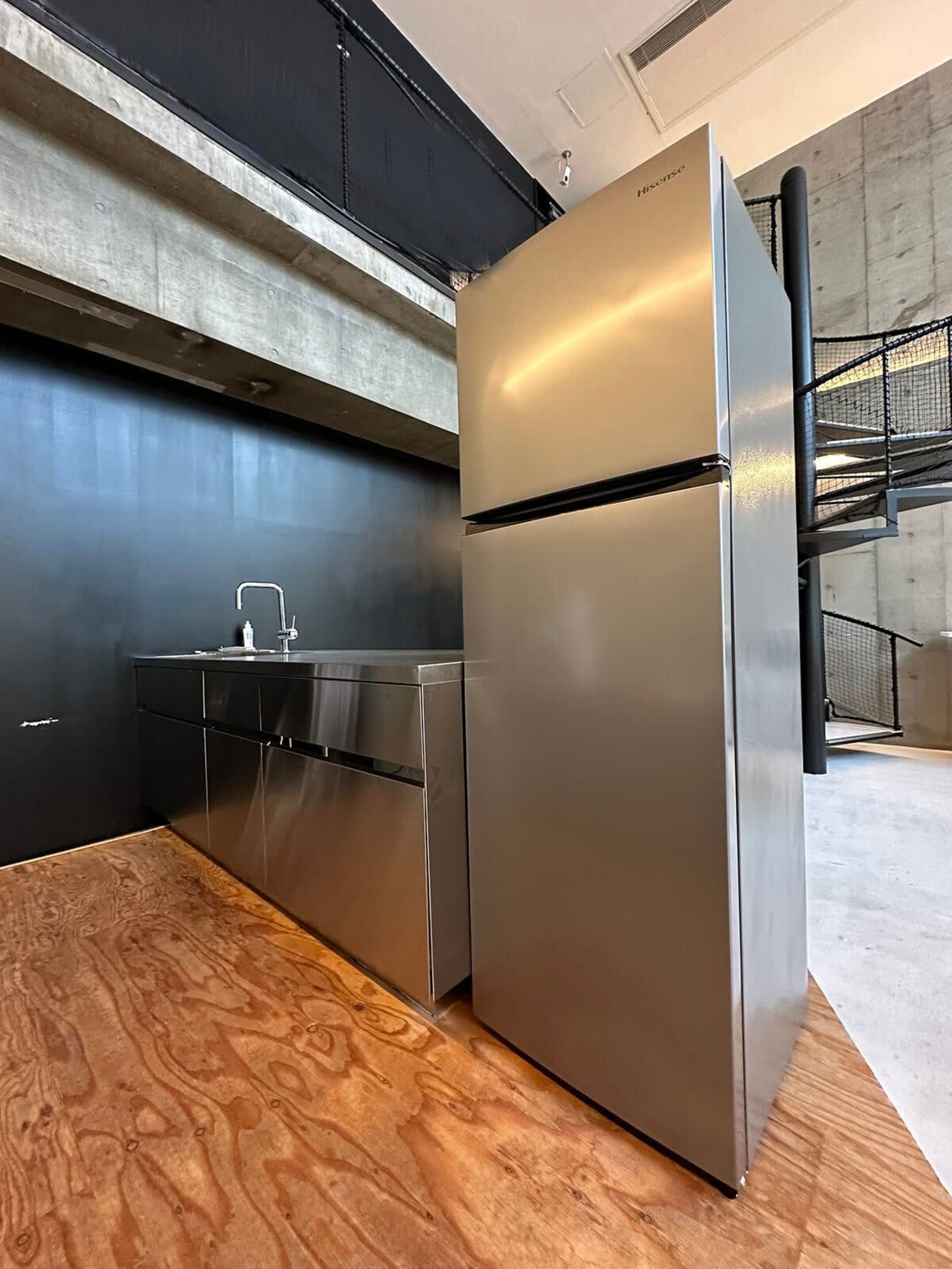 Cozinha moderna com eletrodomésticos de aço inoxidável, bancada de madeira e painel de fundo de concreto.