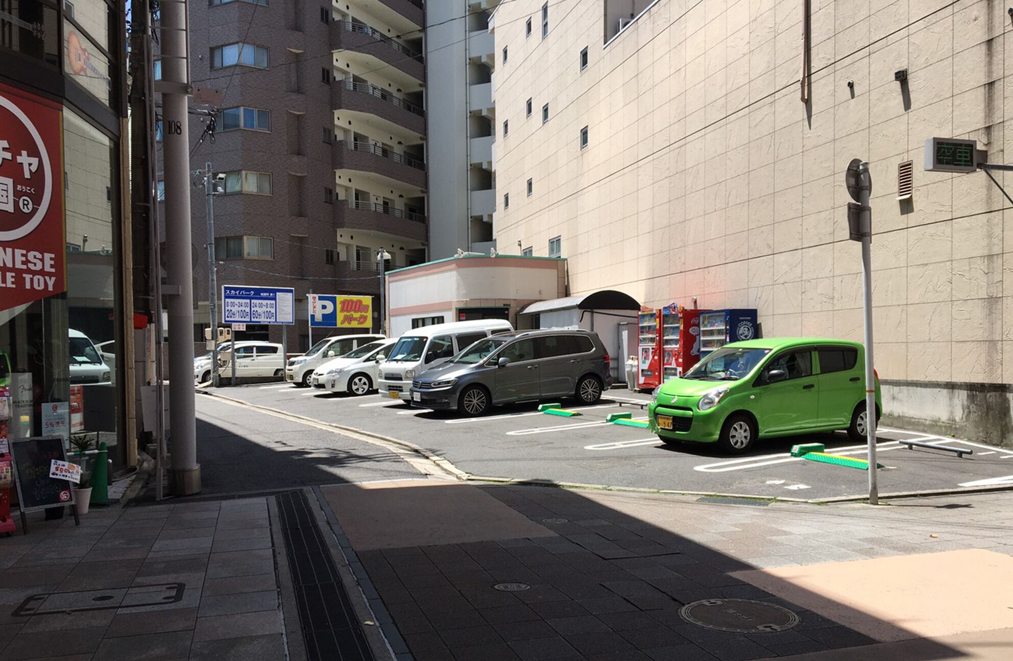 A parking lot with several cars, a building with multiple floors, and a sign indicating parking rates.