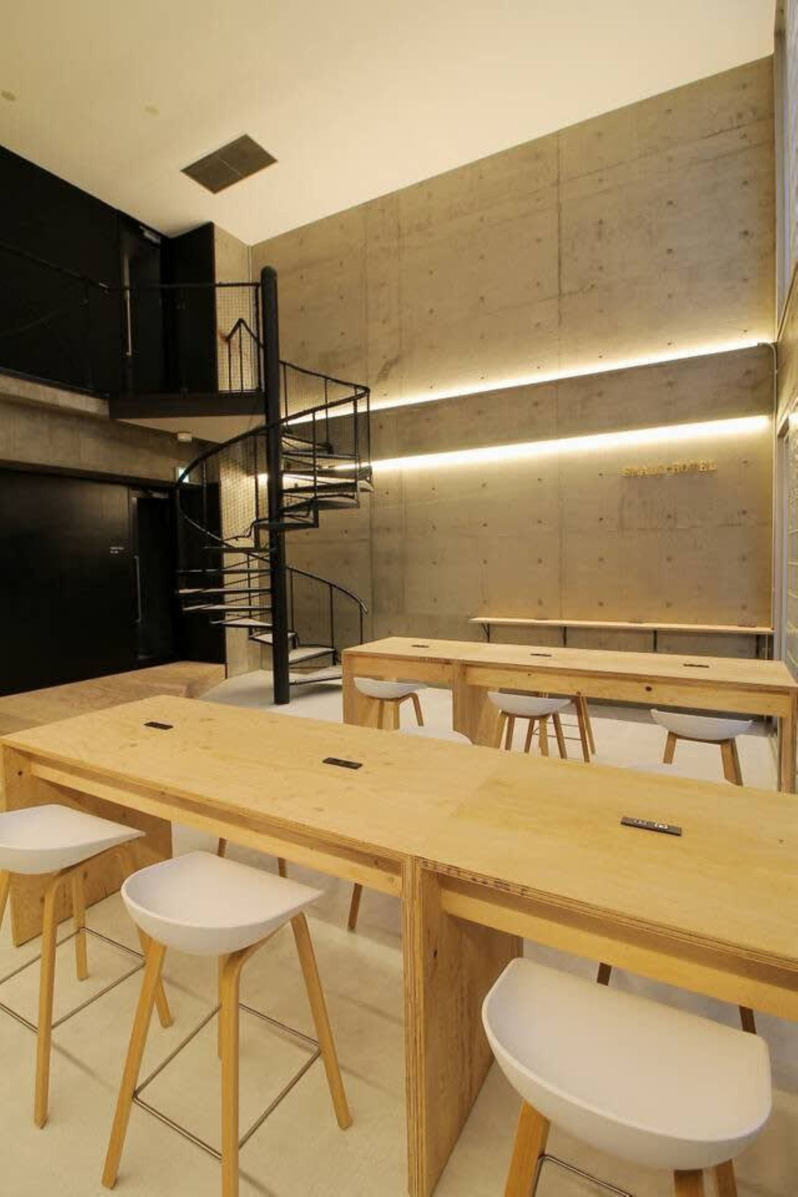 A modern kitchen with a spiral staircase, wooden tables, and white stools.