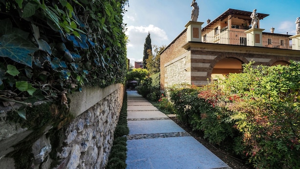 A stone pathway leading to a building with a brick facade and statues on the roof. - Corte Merighi Charming Rooms & Breakfast (Verona)