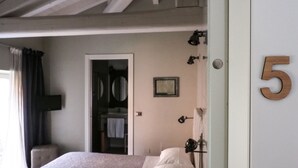 A bedroom with a bed, a door with the number 5, a window with curtains, and a bathroom visible through an open door. - Corte Merighi Charming Rooms & Breakfast (Verona)