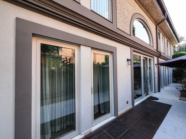 A modern building with large sliding glass doors, a flat roof, and a small outdoor area with a mat and potted plants.