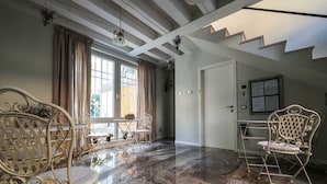 A spacious room with a marble floor, white walls, and a staircase. There are two white metal chairs and a small table with flowers. - Corte Merighi Charming Rooms & Breakfast (Verona)