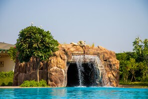 A rock formation with a waterfall and a pool. - The Baagh Ananta Elite (Sawai Madhopur)