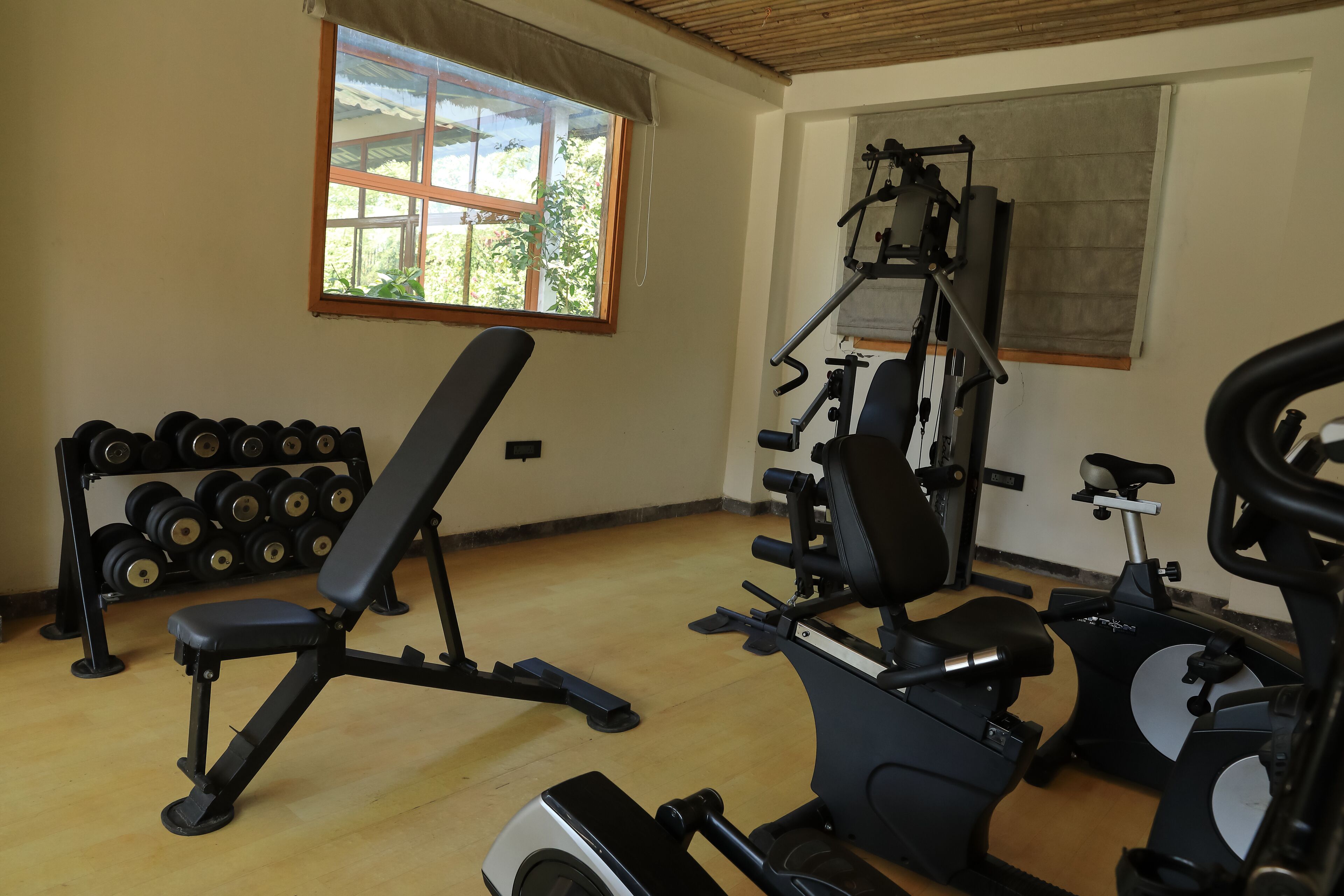 A gym with exercise equipment, a bench, and a rack of dumbbells.