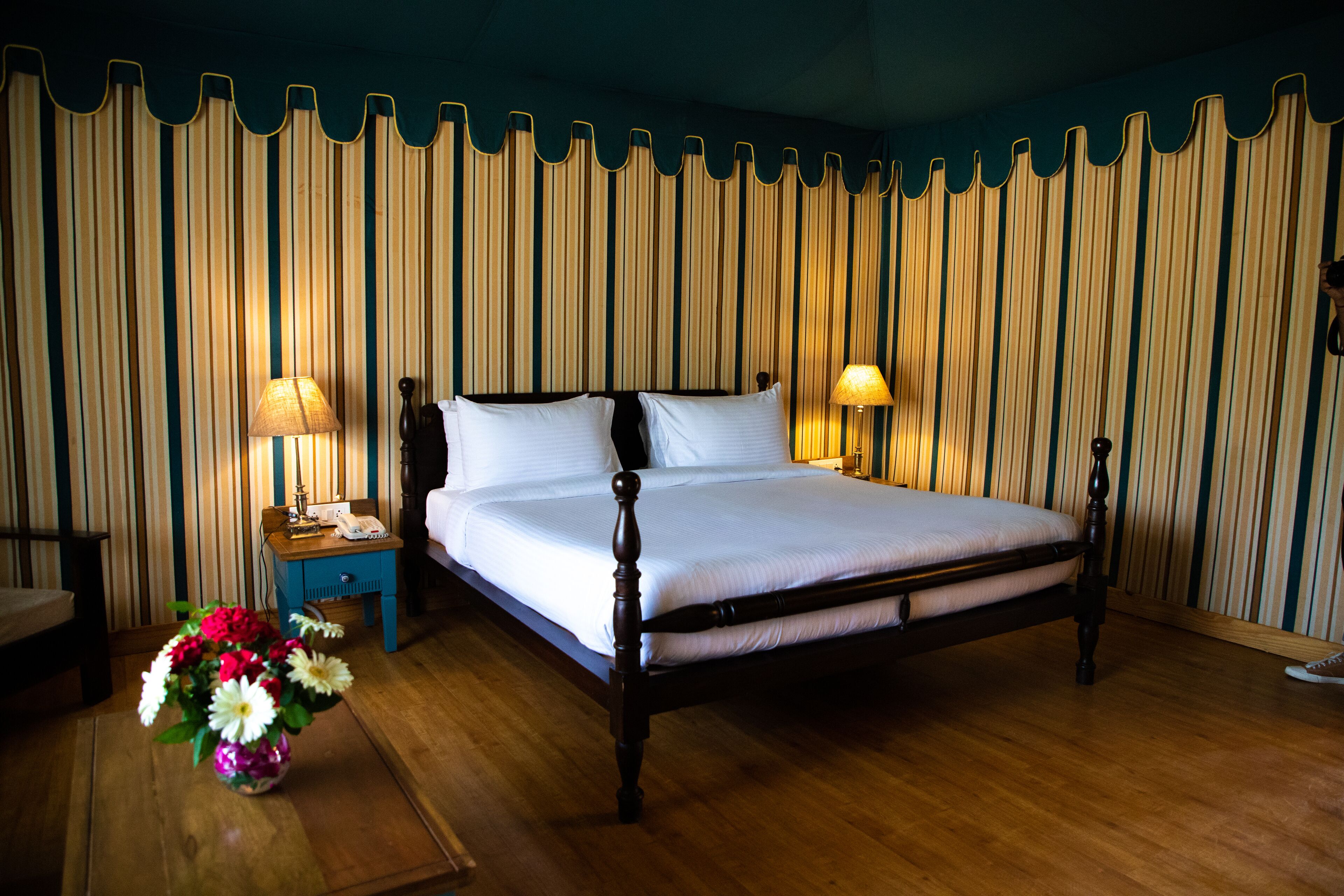 A neatly made bed with a wooden frame, two bedside tables with lamps, and a vase of flowers on the floor.