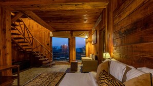 Un interior de madera con una cama, un sofá, una silla, una escalera y vistas al exterior.
