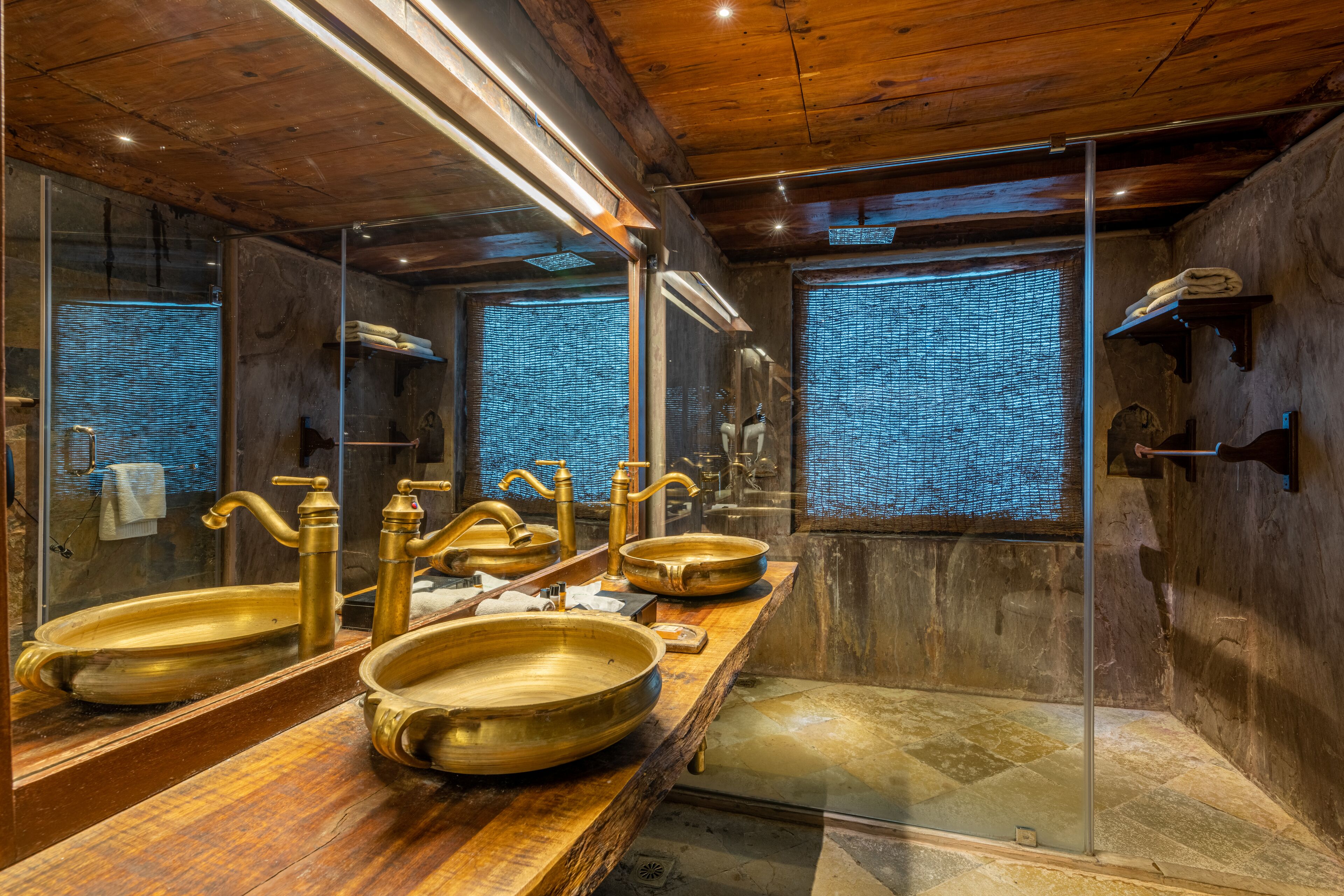 A luxurious bathroom with a large mirror, two gold sinks, and a glass-enclosed shower area.