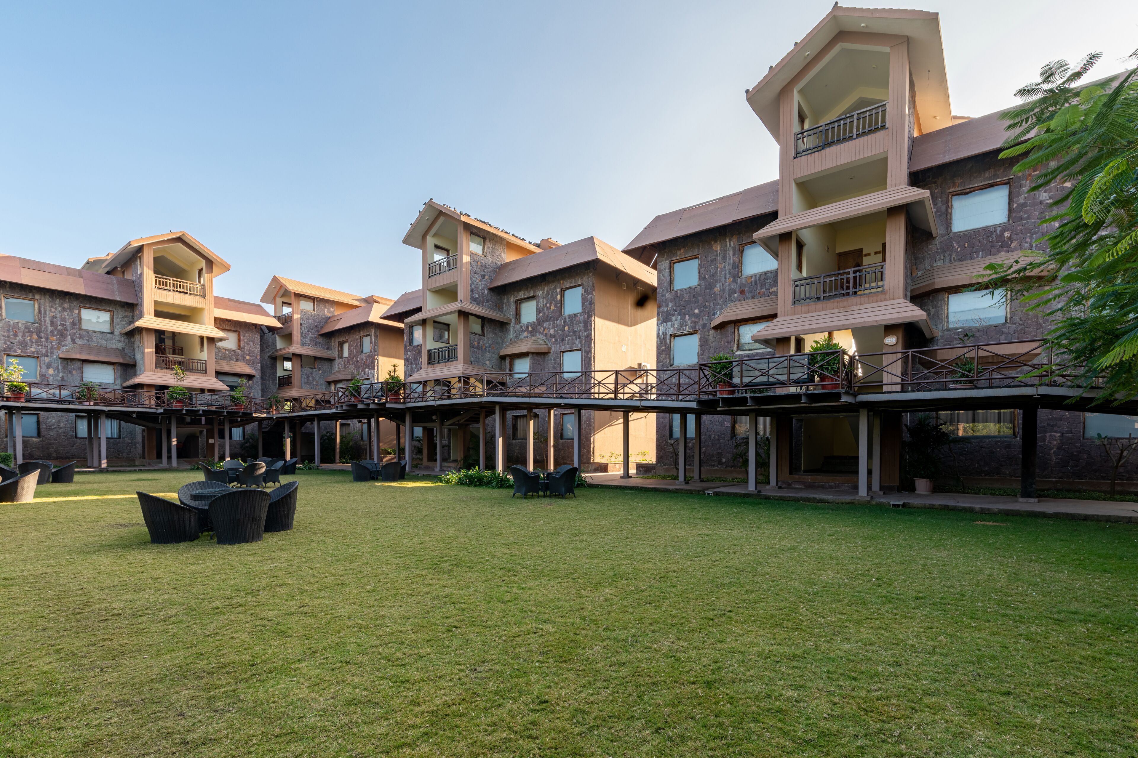 Un hotel moderno de varios pisos con balcones, mobiliario exterior y una terraza cubierta.