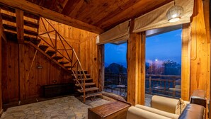 Un interior de madera con piso de piedra, una escalera de madera, un sofá y vistas a través de un ventanal grande.