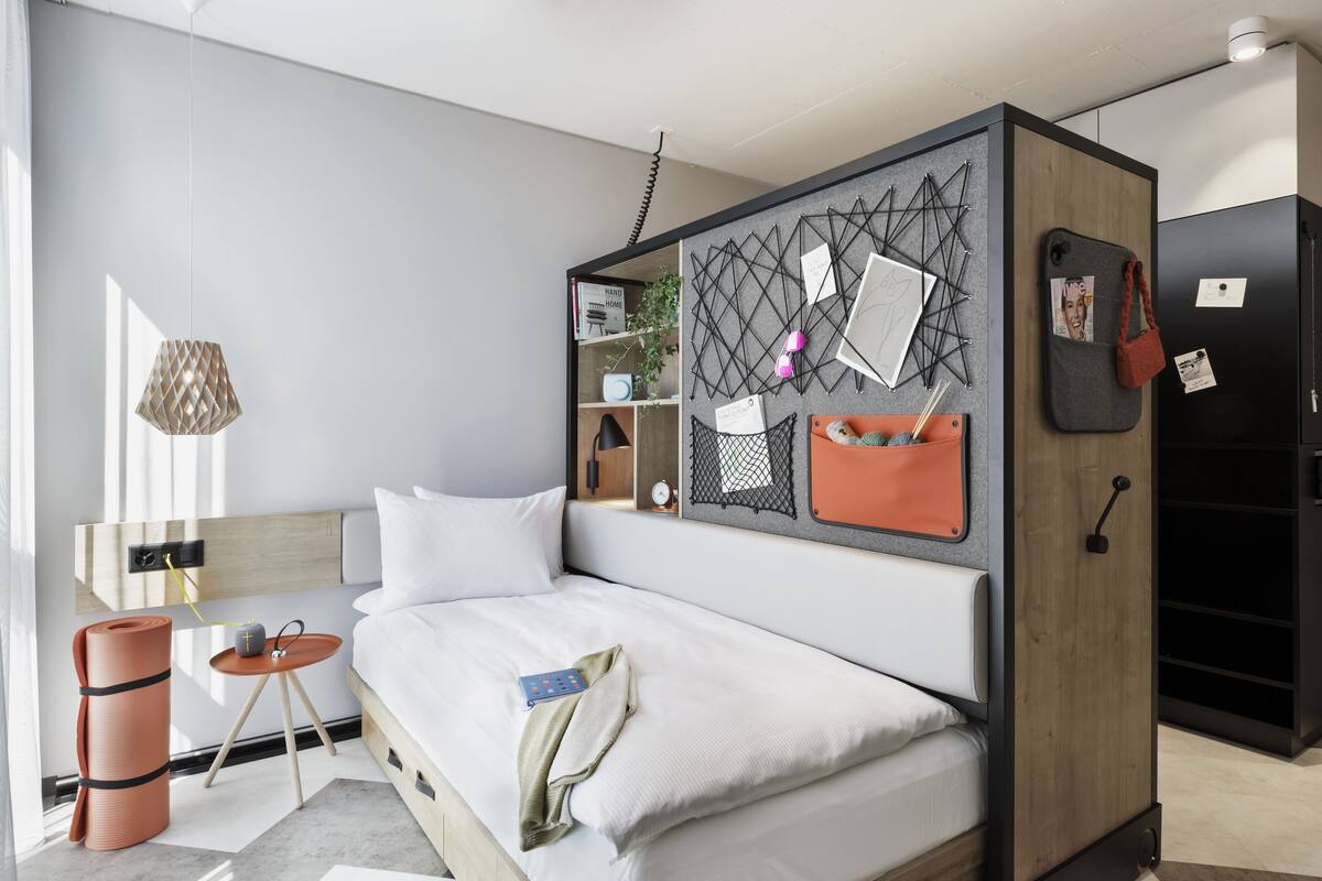 Una habitación de hotel moderna con cama, una mesita, un estante en la pared y un armario.