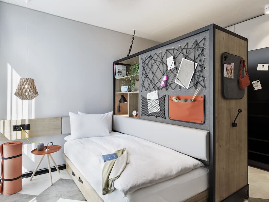Una habitación de hotel moderna con cama, una mesita, un estante en la pared y un armario.