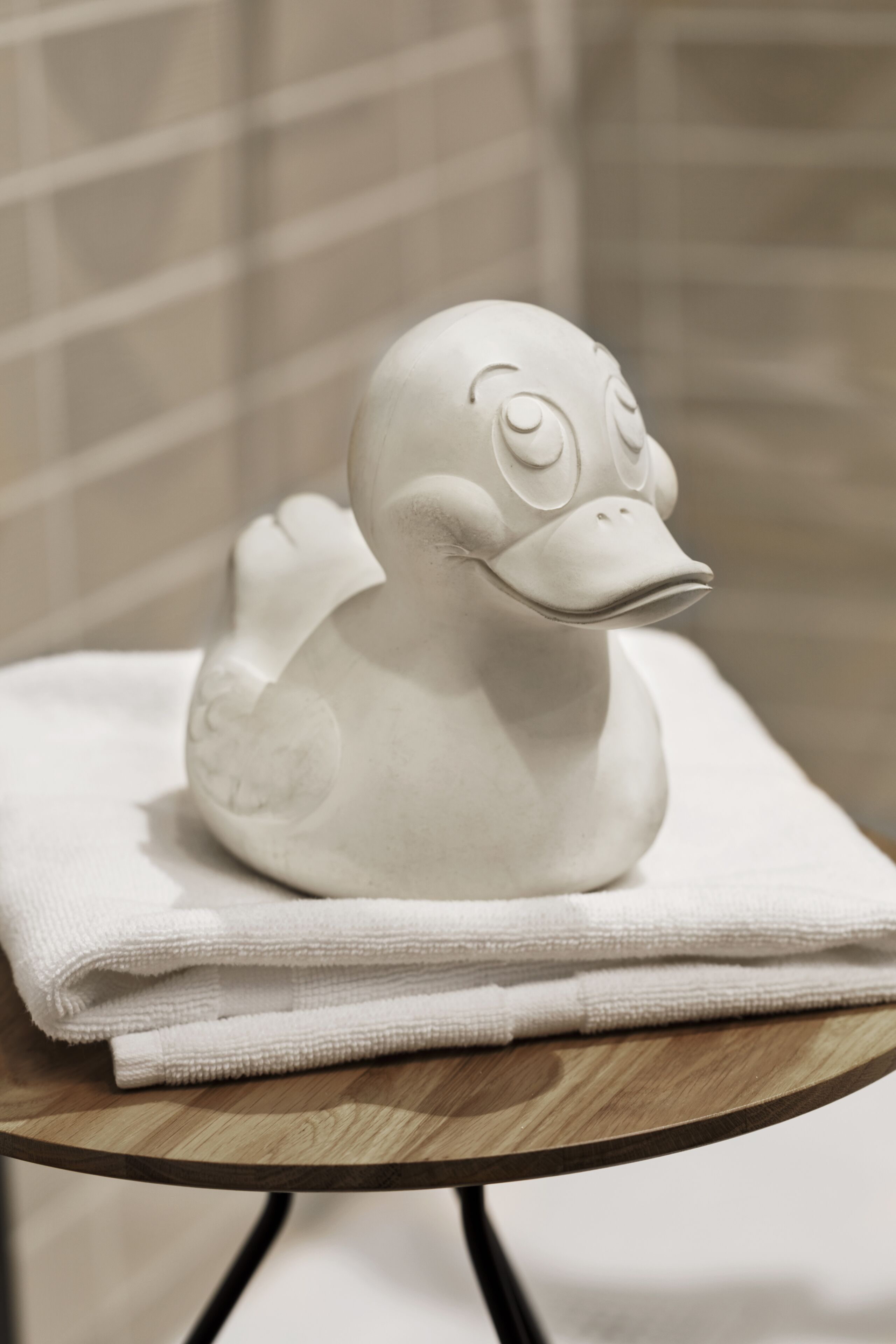 Een keramieken eendbeeldje op een gevouwen witte handdoek op een houten tafel.